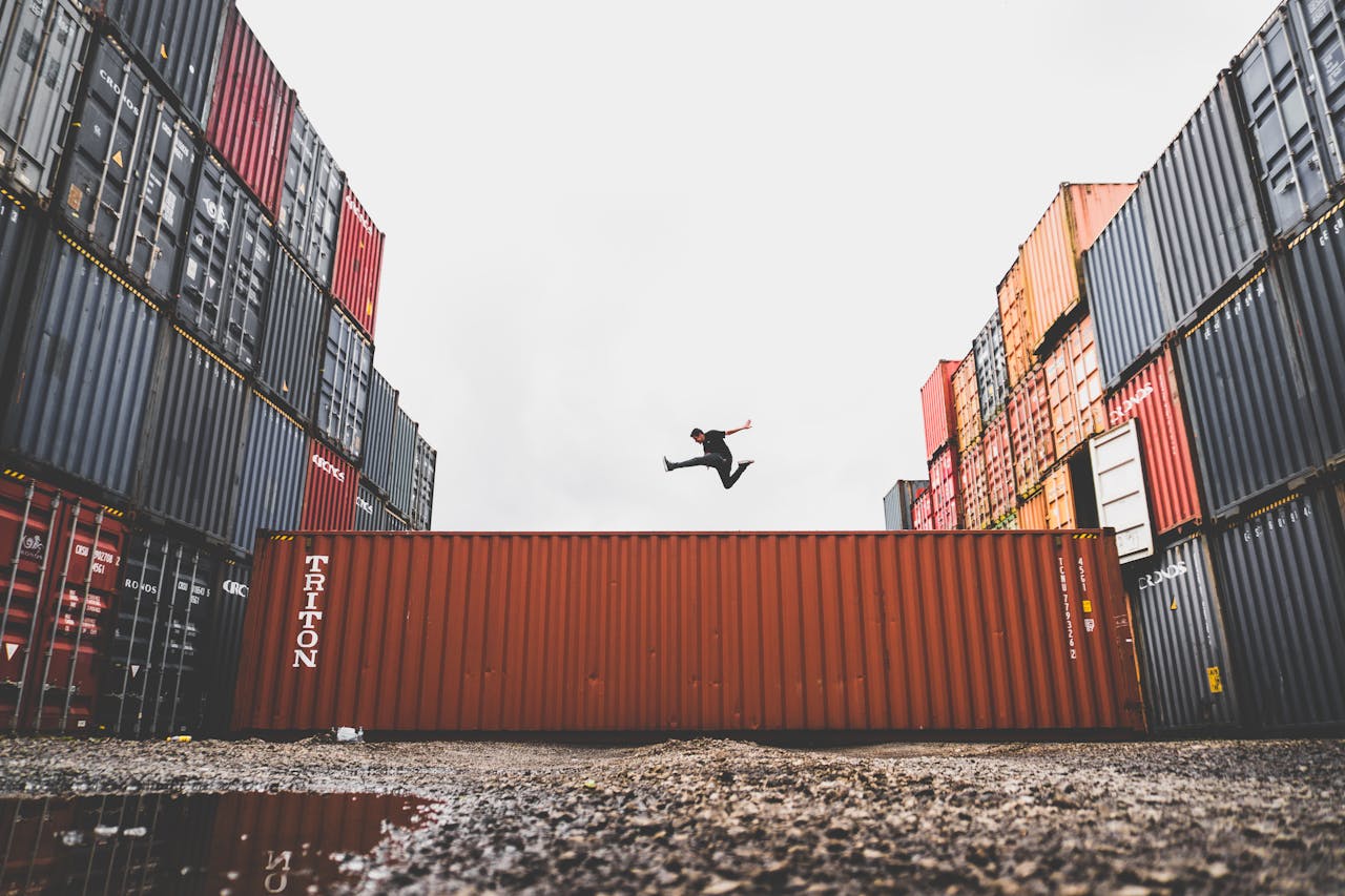 about-01 A person leaps dramatically above stacked shipping containers, showcasing freedom and industrial energy.